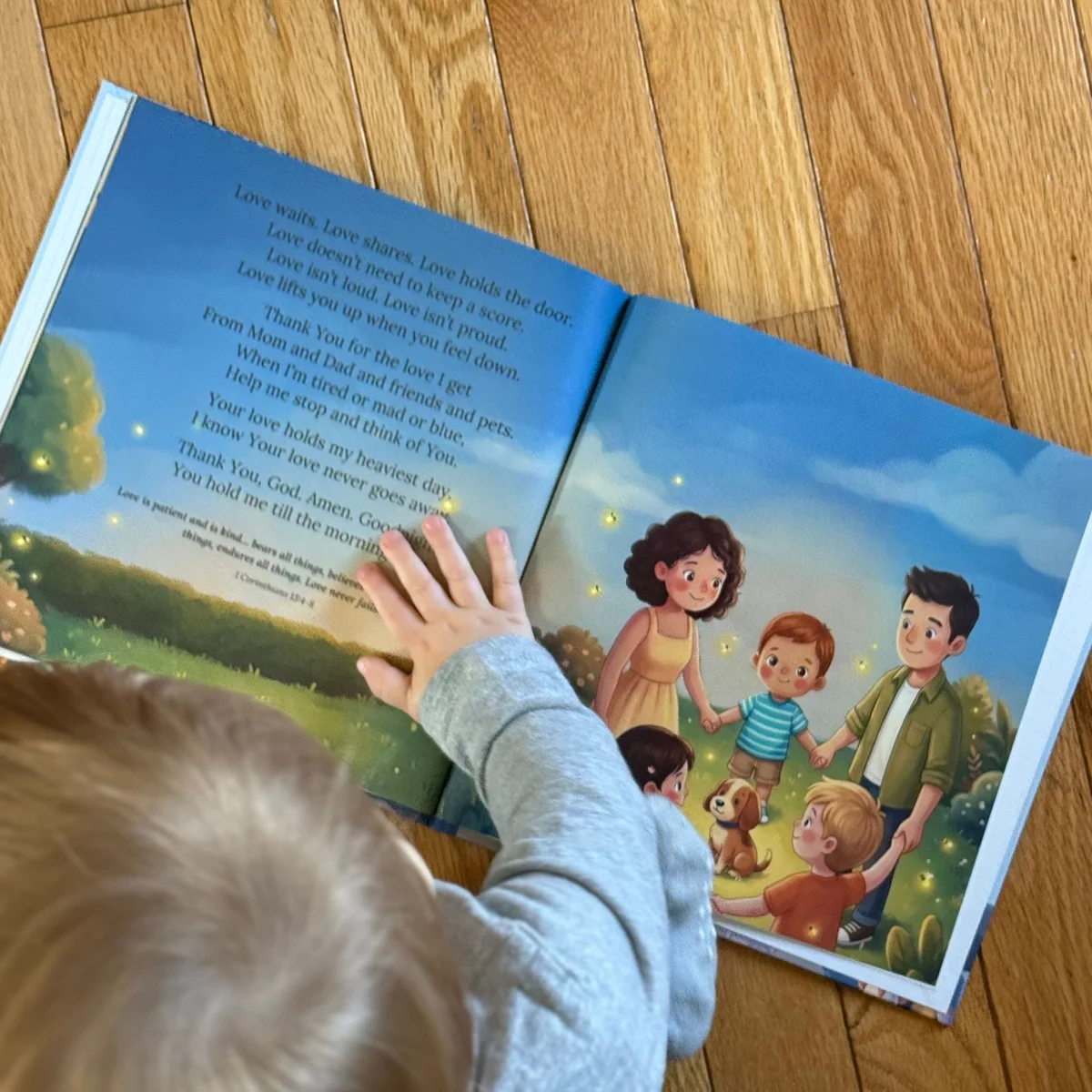 A printed copy of Little Prayers open at the family spread, with a child's hand resting on the page.