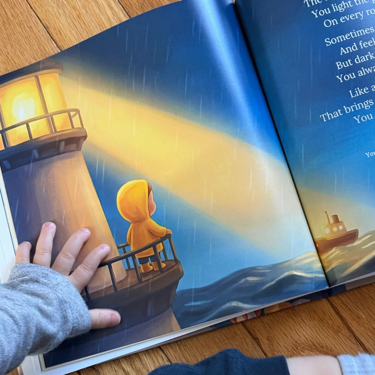 A close-up of the lighthouse illustration in a printed copy of Little Prayers, with a small hand on the page.